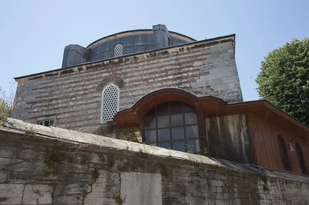 Haseki Sultan Camii'nin taş duvarının üstünde yükselen kubbe kasnağı, pencereler ve duvara eklenmiş ahşap bir bölme.