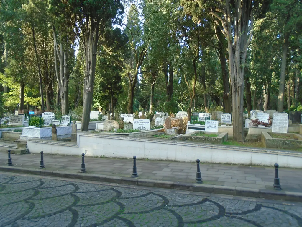 Karacaahmet Mezarlığı'nda kabir adası; alçak taş duvarlı alan içinde beyaz mezar taşları, babalar ve selviler.
