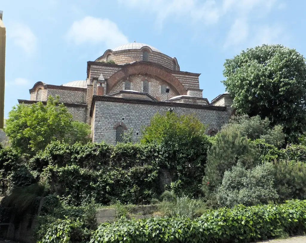 Rum Mehmed Paşa Camii'nin genel görünümü; yeşil bahçenin ardında taş-tuğla duvarlar, yarım kubbe ve ana kubbe.