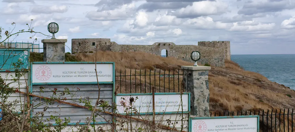 Rumeli Feneri Kalesi 2025'te; kuru otlarla kaplı yamaçta taş surlar, önde bakanlık panolarıyla kaplı çit.