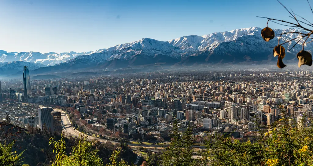 Cerro San Cristóbal'dan Santiago; ufku boydan boya kaplayan karlı And duvarı ve önünde uzanan şehir dokusu.