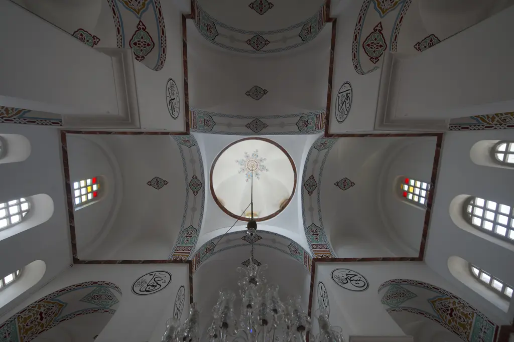 Bodrum Camii'nin kubbesine dik yukarı bakış; göbekte kalem işi rozet, dört yöne açılan beşik tonozlu haç kolları, köşelerde hat madalyonları ve vitraylı pencereler.