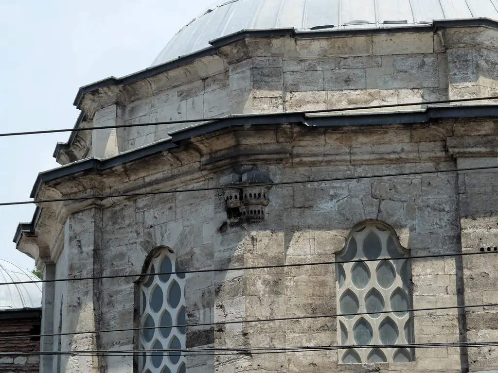 III. Mustafa Türbesi'nin dış görünümü; çok kenarlı taş gövde, iki sıra şebekeli pencere, profilli saçak ve üstte kubbe.