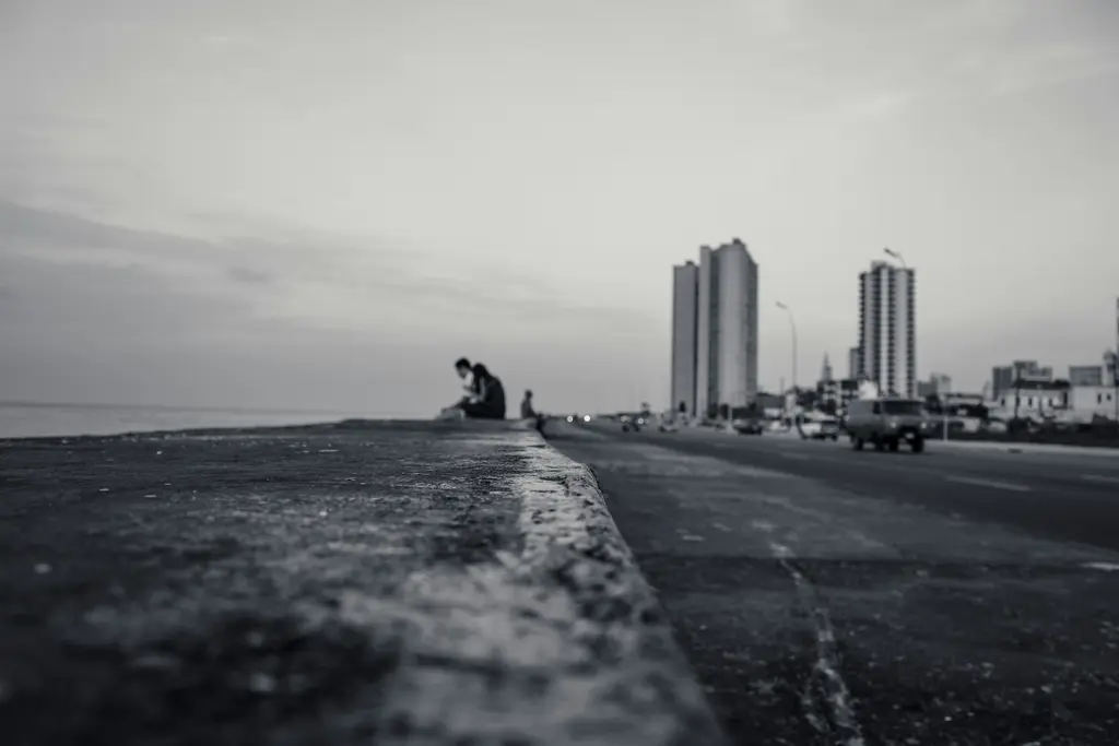 Havana'da Malecón sahil duvarı; boydan boya uzanan beton set, duvarın üstünde oturan tek bir kişi ve arkada yükselen şehir binaları.