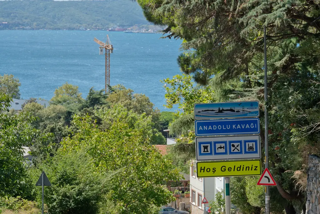 Anadolu Kavağı'nın girişinde mavi tabela ve "Hoş Geldiniz" levhası; arkada ağaçlar ve mavi Boğaz suyu.