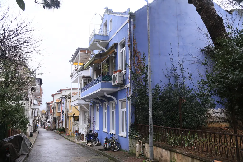 Büyükada'da sokak; mavi cepheli evler, balkonlar, park edilmiş bisikletler ve dar asfalt yol.