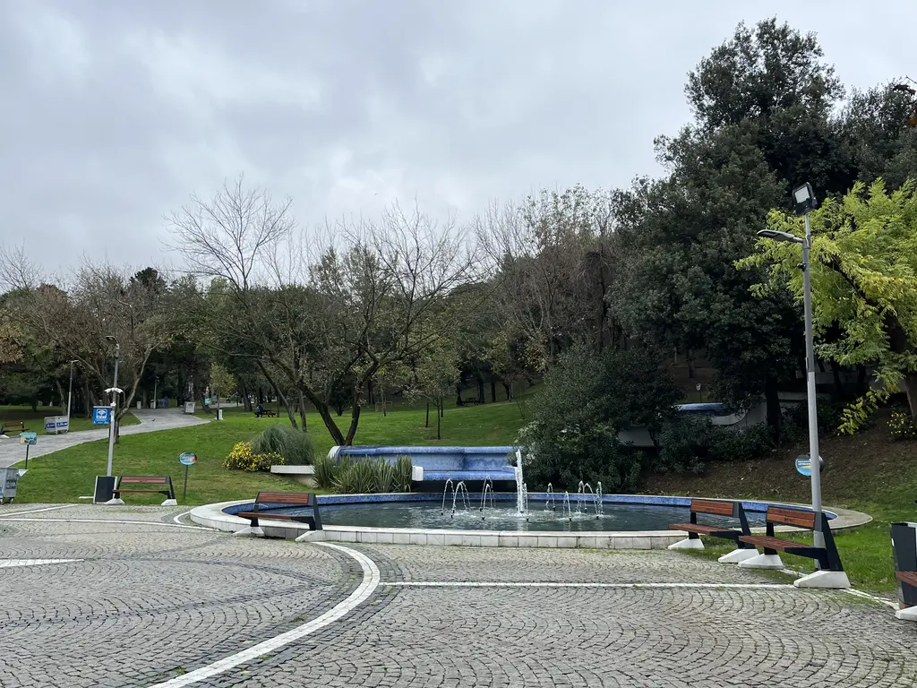 Maçka Demokrasi Parkı'nda desenli parke taşlı meydan; alçak fıskiyeli dikdörtgen havuz, banklar, arkada çimenlik ve ağaçlar.