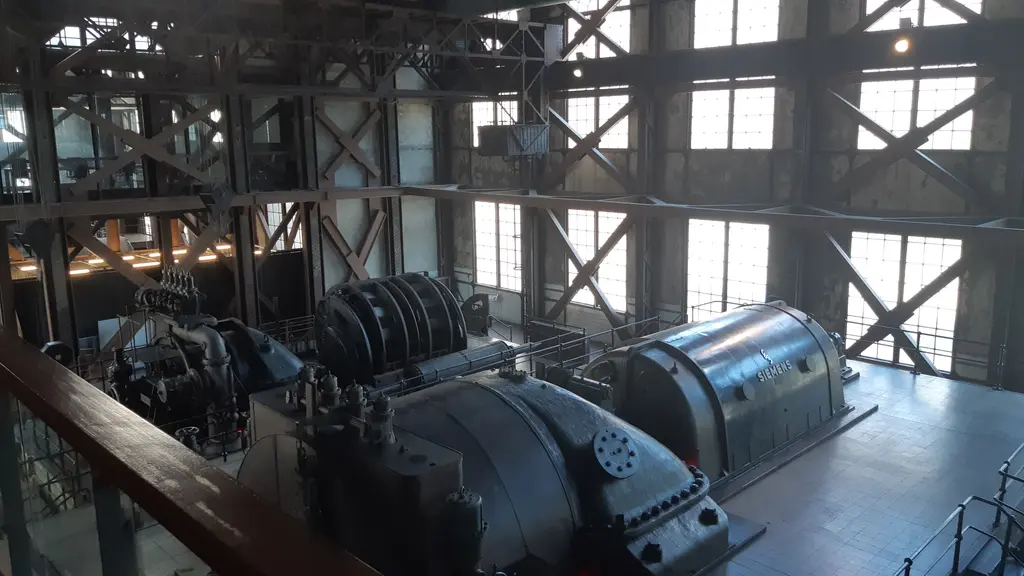 Enerji Müzesi'nde jeneratör grupları; mavi-gri boyalı iri makineler, korkuluklu platformlar, çelik çerçeveli büyük pencereler.