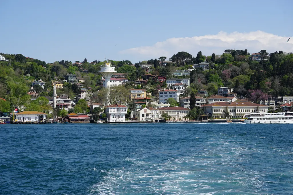 Boğaz'dan Kanlıca; kıyıda yalılar ve vapur, yamaçta ağaçlar arasında evler, minare ve beyaz radar kulesi.