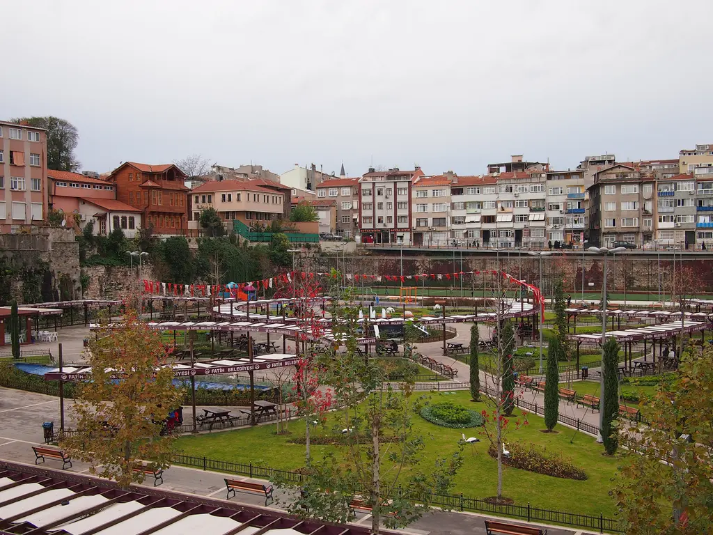 Caminin batısındaki Çukurbostan; dev dikdörtgen çukurun içinde yürüyüş yolları, çim alanlar ve fidanlar, çevresinde apartmanlarla ahşap evler.