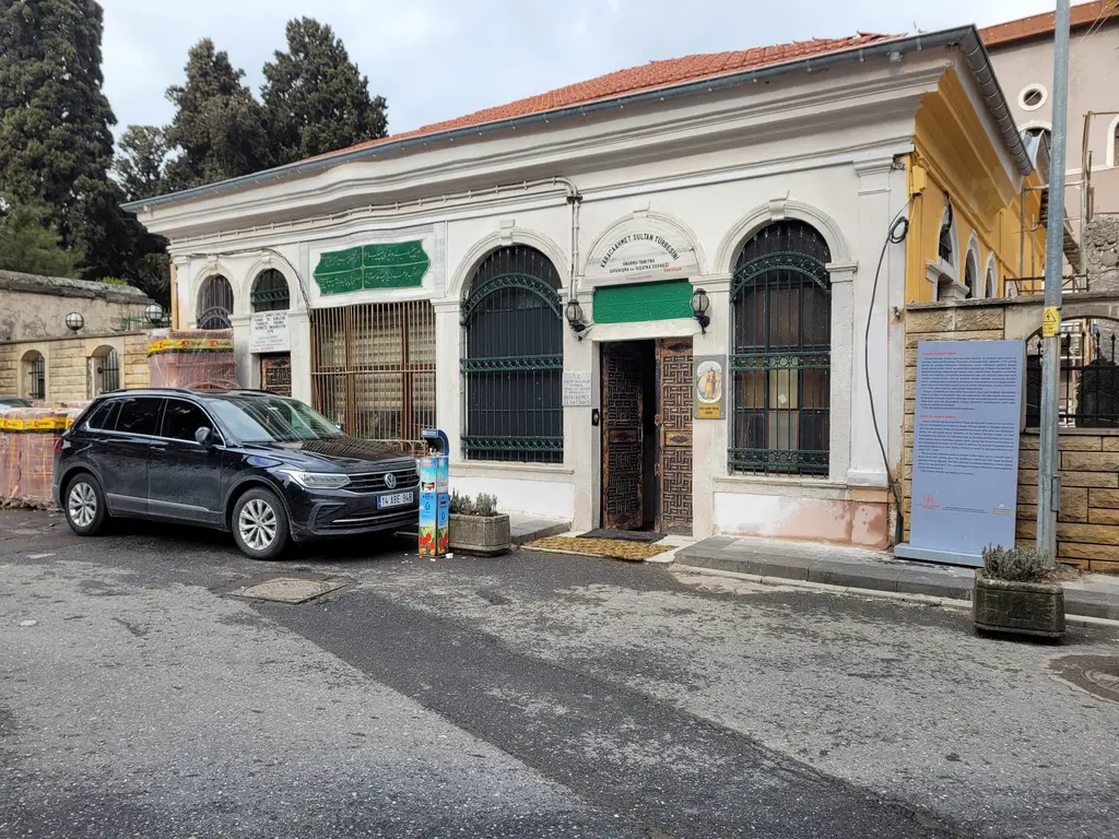 Karaca Ahmed Sultan Türbesi'nin cephesi; pembe ve beyaz sıvalı duvar, kemerli pencereler, giriş kapısı ve önünde bilgi panosu.