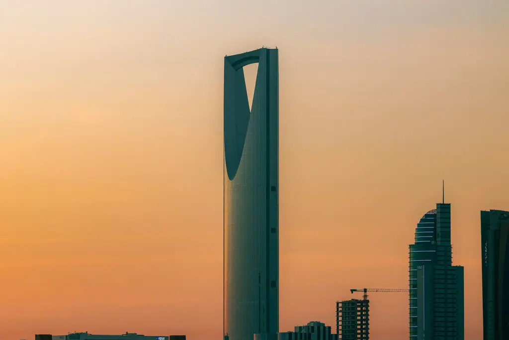 Riyad'da gün batımında Kingdom Centre; tepesindeki dev açıklık ve gökyüzü köprüsü, turuncuya dönen gökyüzü ve yanında sıralanan diğer gökdelenler.