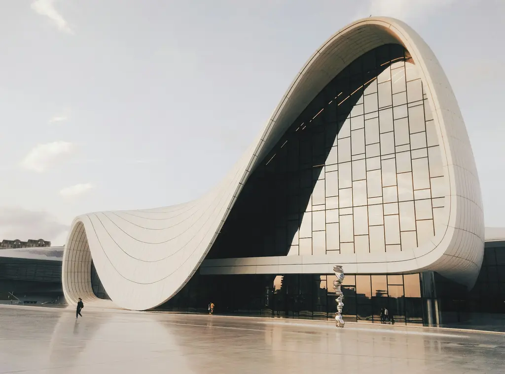Bakü'de Haydar Aliyev Merkezi; dalga gibi akan beyaz kavisli cephesi ve cam yüzeyleri, geniş boş meydanda birkaç yaya.