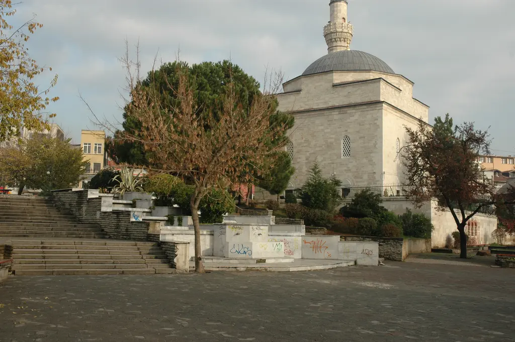 Firuz Ağa Camii'nin yanındaki basamaklı yeşil set; taş merdivenler, ağaçlar, çalılar ve arkada kubbe ile minare.