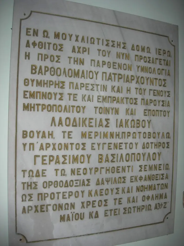 Kanlı Kilise'de beyaz mermer levha üzerinde büyük harflerle yazılmış Yunanca kitabe; yaldızlı harfler ve düz kenarlı çerçeve.