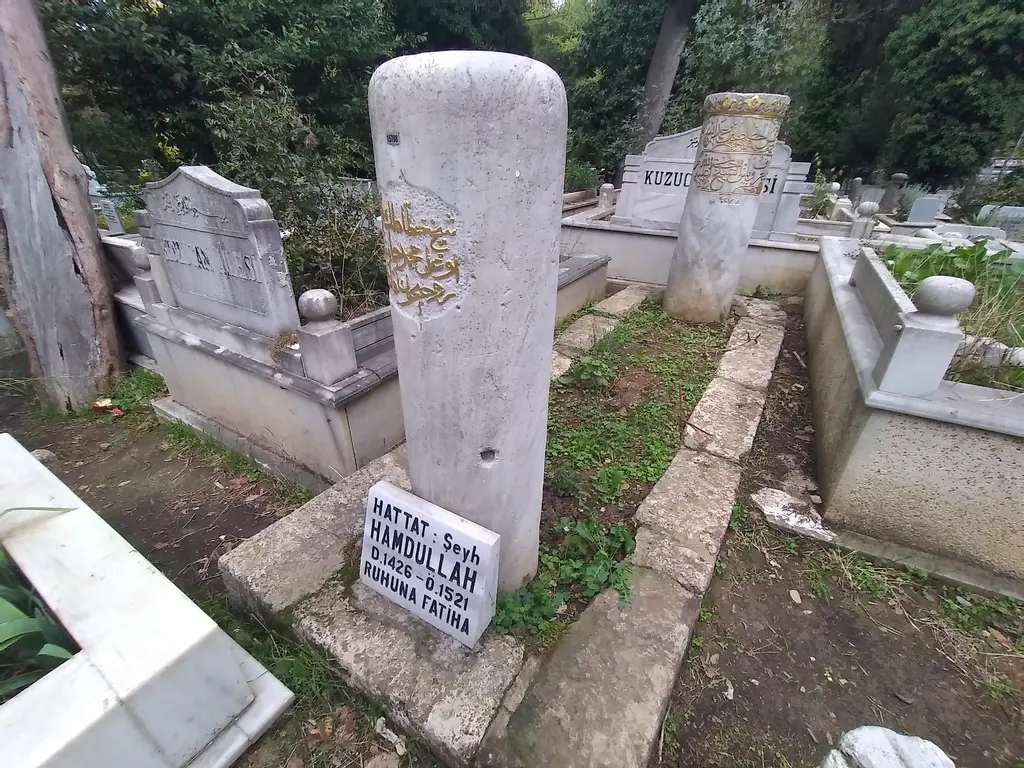 Karacaahmet'te hattat Şeyh Hamdullah'ın kabri; altın yaldızlı yazılı silindir mezar taşı, önünde levha ve çevresinde kabirler.