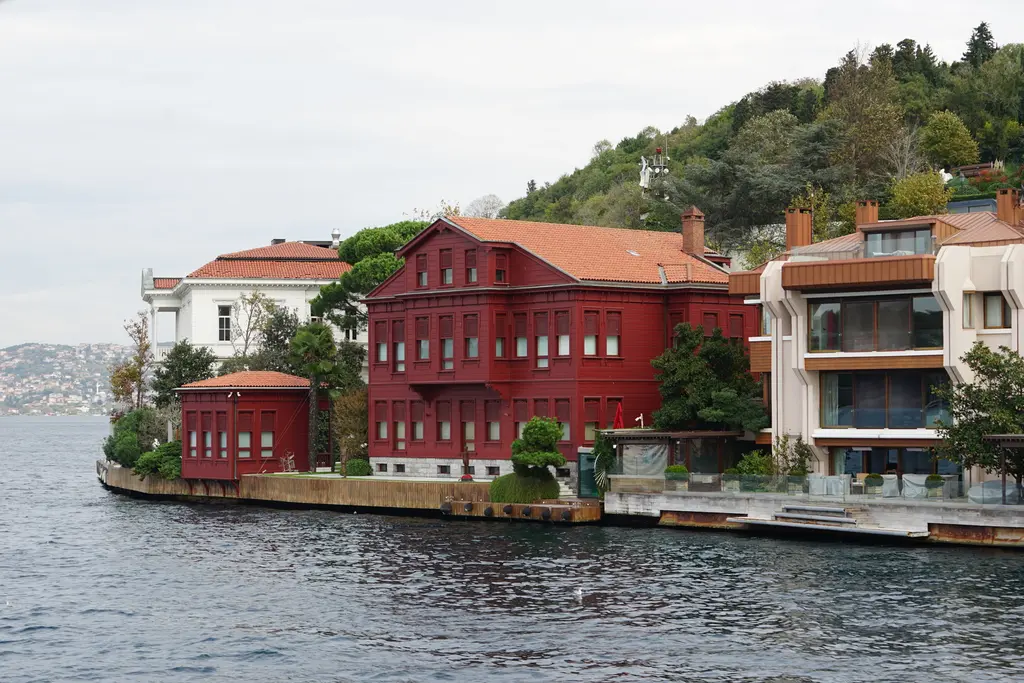 Yedi Sekiz Hasan Paşa Yalısı; koyu kırmızı ahşap cephe, kiremit çatı, yanında beyaz yalılar ve önde rıhtım.