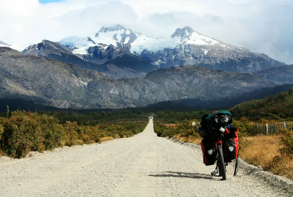 Carretera Austral; çakıl yolda park etmiş yüklü bir gezi motosikleti, ilerideki ormanlık yamaçlar ve karlı dağlar.