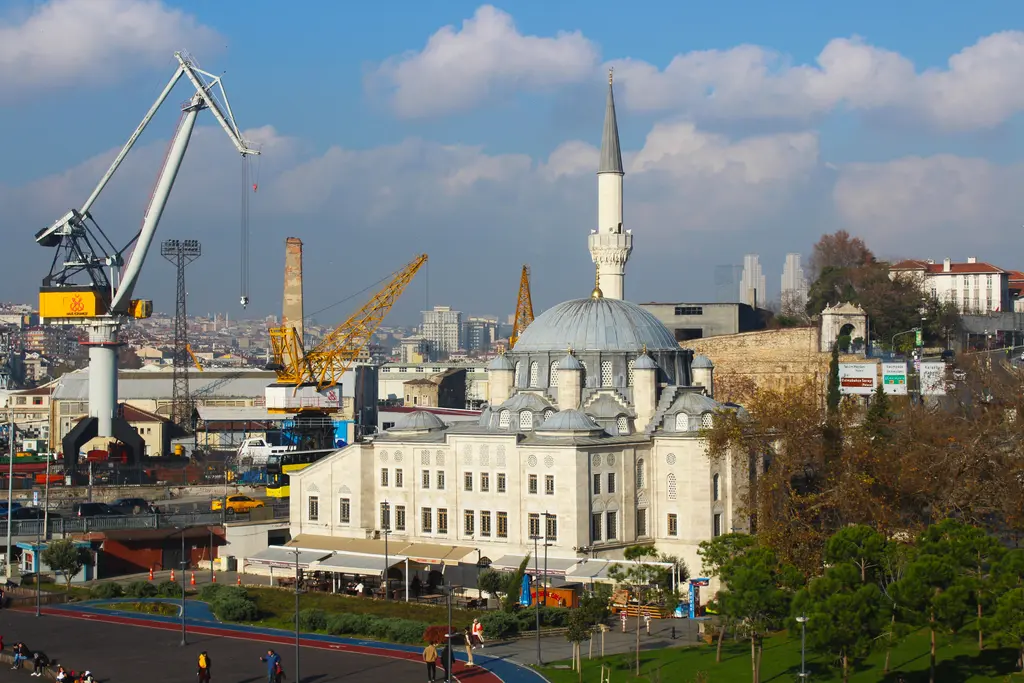 Azapkapı Sokullu Mehmed Paşa Camii; beyaz taş gövde ve kubbe, ince minare, arkada sarı tersane vinçleri ve önde sonbahar ağaçları.