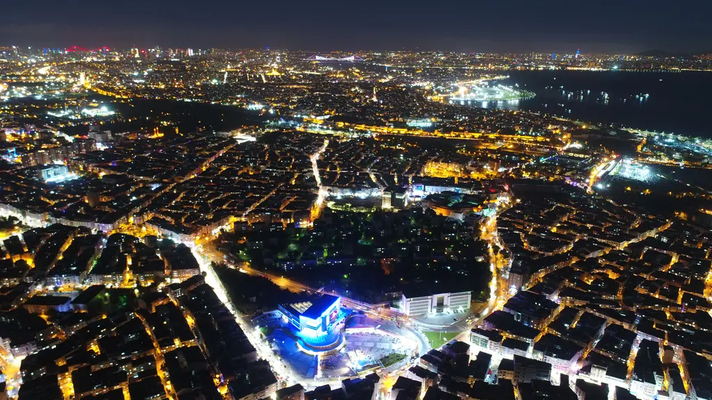 Gece havadan Zeytinburnu; ışıklı sokak ızgarası boyunca sık apartman blokları, ortada aydınlatılmış bir meydan ve arkada Marmara Denizi'nin karanlık şeridi.