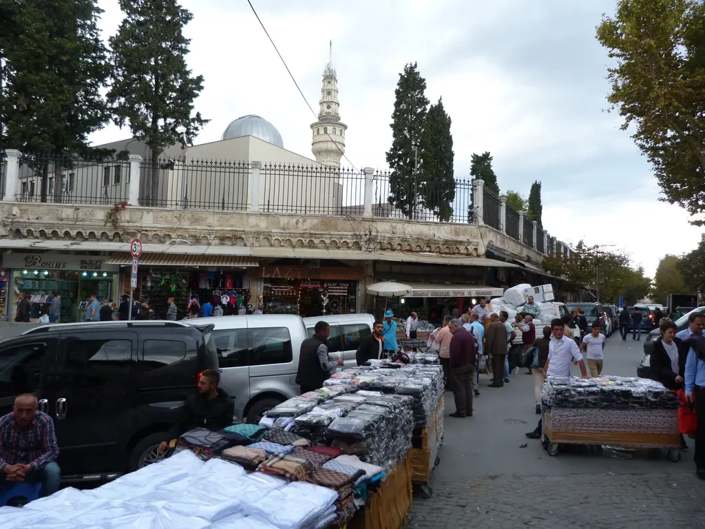 Beyazıt'ta kule ve çevresi; cadde boyunca dizilmiş tekstil tezgâhları, kalabalık kaldırım, kampüs duvarı ve arkada kulenin üst bölümü.