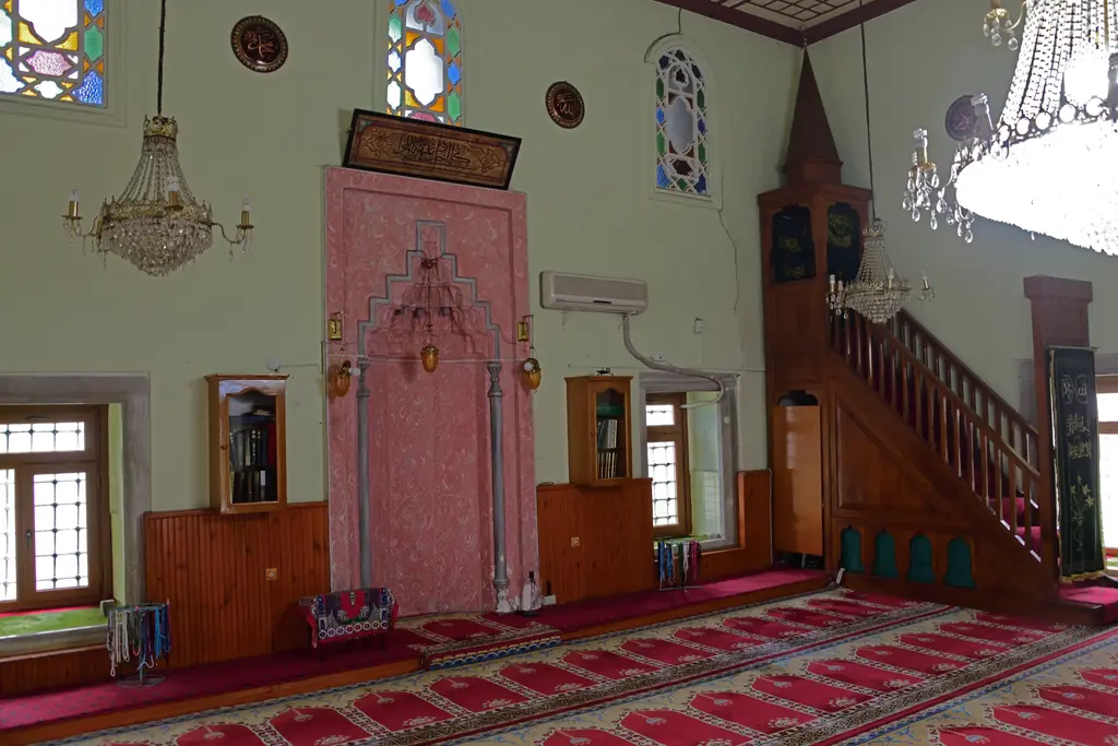 Defterdar Camii'nde mihrap ve minber; pembe mermer mihrap nişi, ahşap minber merdiveni, kemerli pencereler ve avize.
