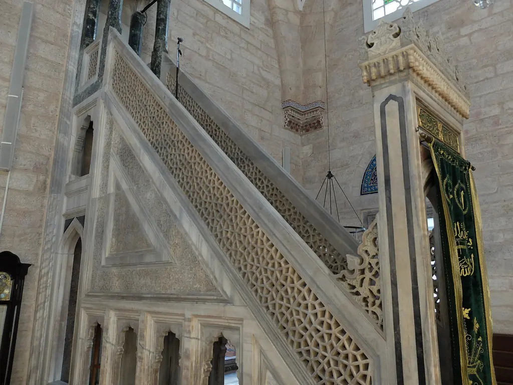 Yavuz Sultan Selim Camii'nin minberi; beyaz mermerde şebekeli korkuluk, basamak dizisi, yan aynalıktaki kabartma ve sağda yeşil sancak.