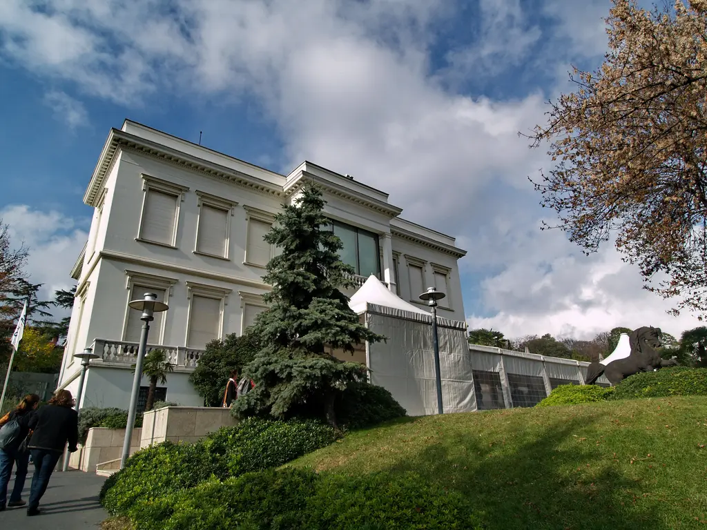 Sakıp Sabancı Müzesi; sağda beyaz Atlı Köşk, solda camlı modern galeri bölümü, çimenli yamaç ve bulutlu gökyüzü.