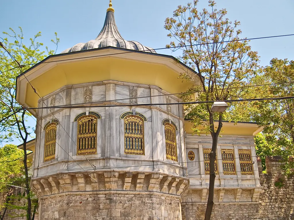 Alay Köşkü'nün soğan kubbesi; kurşun kaplı dilimli külah, geniş saçak, altın sarısı şebekeli pencereler ve iki yanda yeşil ağaçlar.