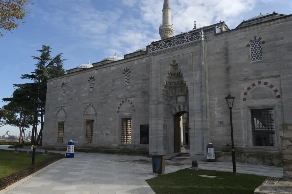 Yavuz Sultan Selim Camii'nin dış duvarı; ortada mukarnaslı taç kapı, kırmızı beyaz almaşık kemerli pencereler, üstte minare ve önde taş döşeli yol.