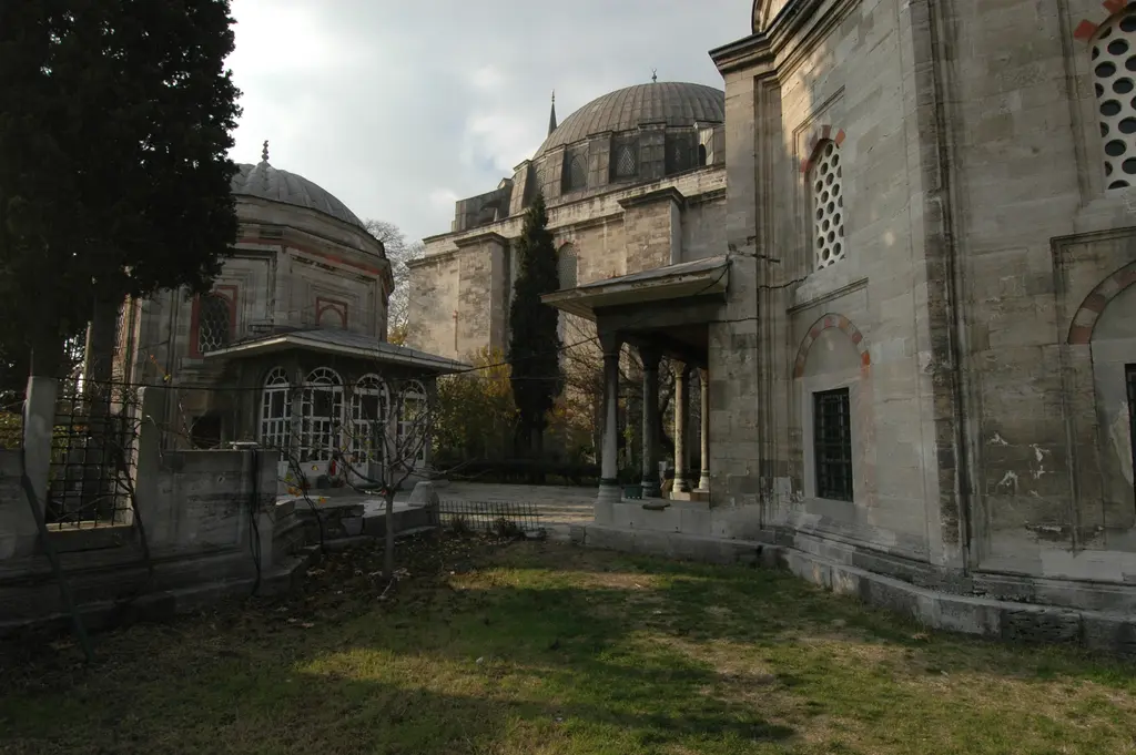 Yavuz Sultan Selim Camii'nin haziresinde iki türbe; solda kubbeli sekizgen türbe, sağda ikinci türbenin taş cephesi, aralarında serviler ve çimen.
