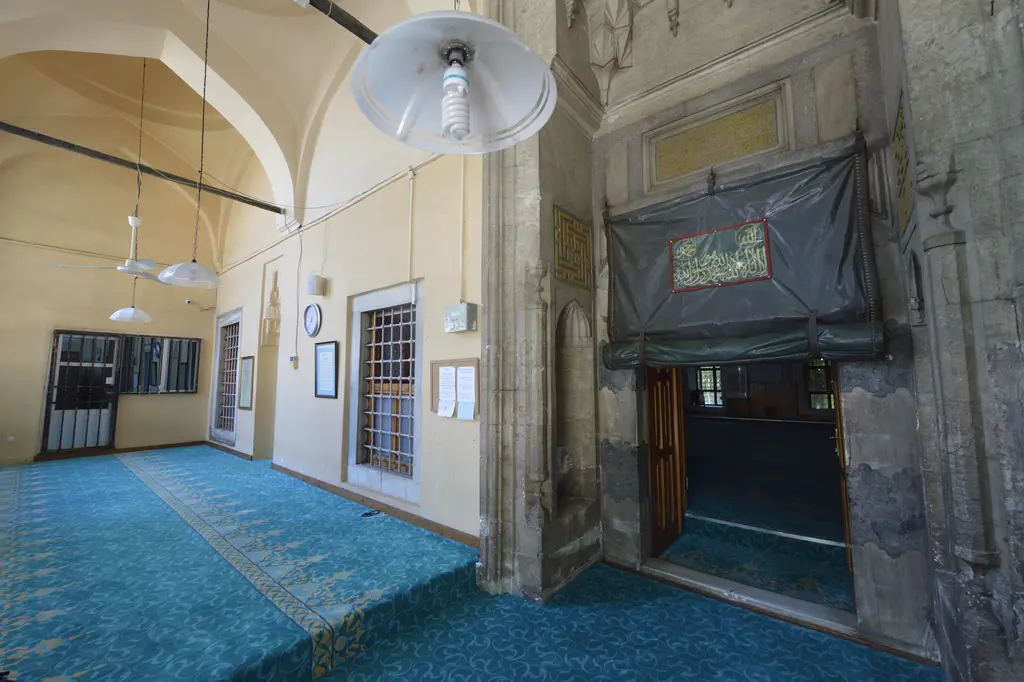 Haseki Sultan Camii'nin kapatılmış son cemaat yeri; mavi halı, sivri kemerli giriş, üstünde yazı levhası, pencereler ve lambalar.