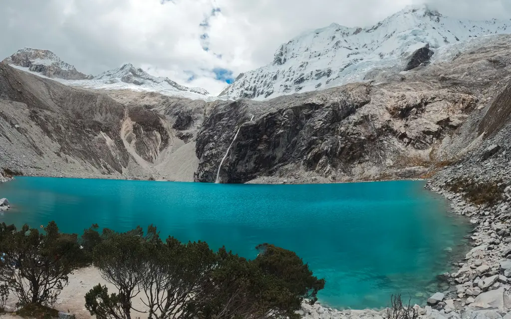 Cordillera Blanca'da buzul gölü; turkuaz renkli göl, dik kayalık yamaçlar ve karlı zirveler.