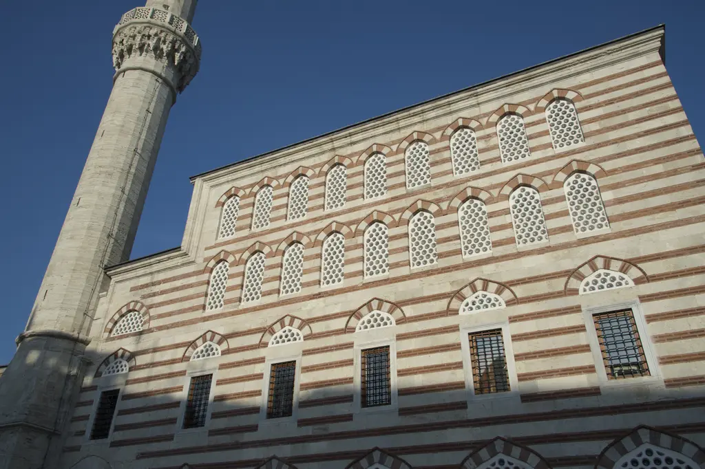 Zal Mahmud Paşa Camii'nin yan cephesi; taş ve tuğla sıralı duvar, dört sıra kemerli pencere, ince minare ve koyu mavi gökyüzü.