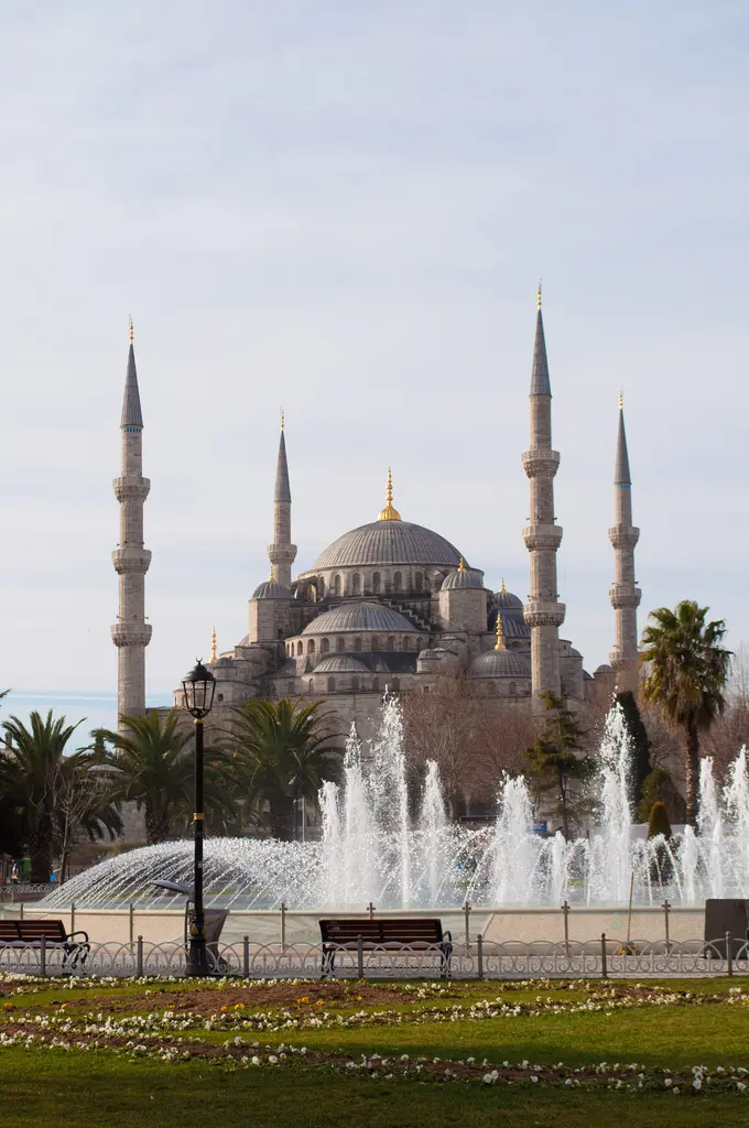 Sultanahmet Meydanı'ndan Sultanahmet Camii; önde fıskiyeli havuz, palmiyeler ve çimenler, arkada altı minare ile kubbeler.