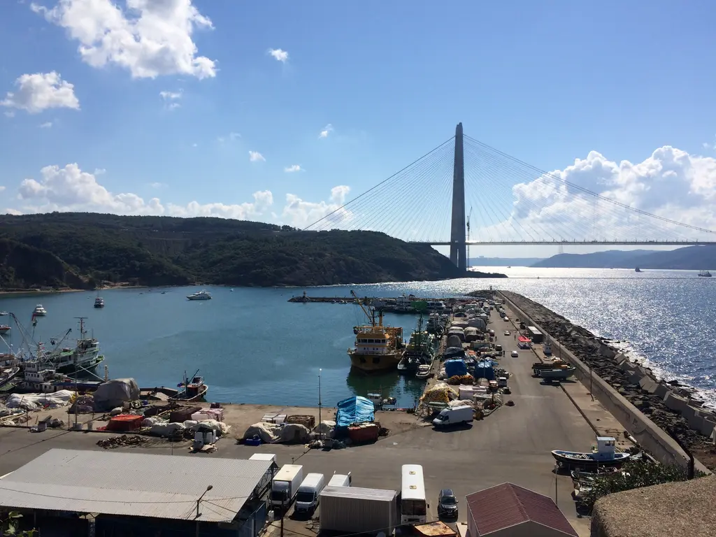 Poyrazköy'de liman; mendirekte balıkçı tekneleri, kıyıda yapılar ve uzakta Yavuz Sultan Selim Köprüsü.