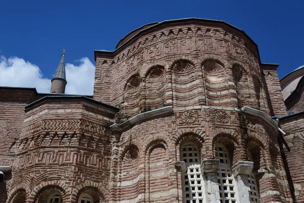 Fenari İsa Camii'nin doğu ucundaki çokgen apsisler; üst üste iki sıra kör kemer, yatay tuğla taş bantlar, mermer şebekeli pencereler ve solda minare külahı.