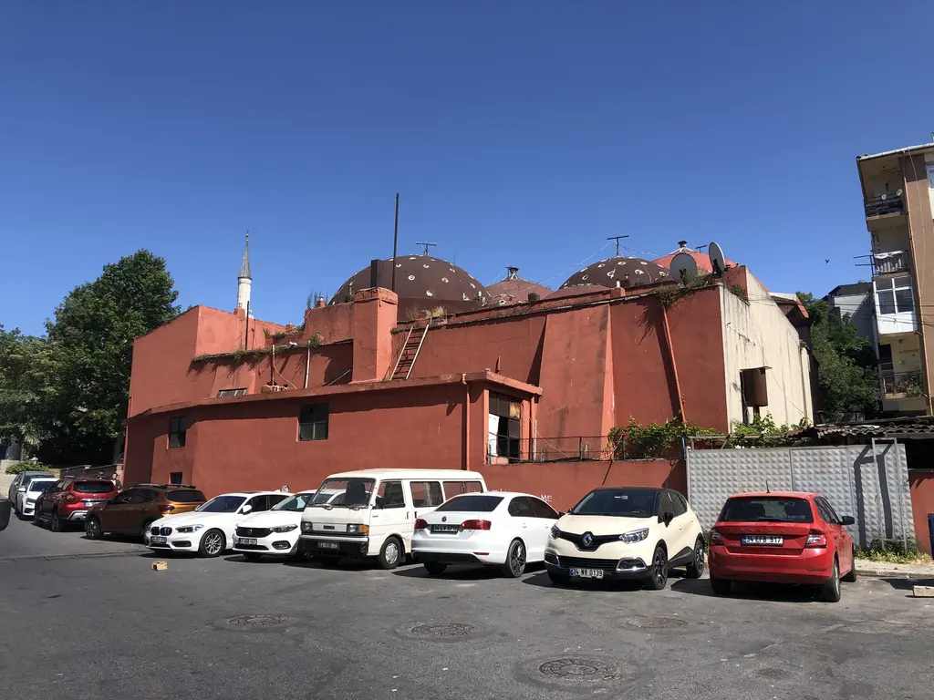 Üsküdar'da Çinili Hamam; kiremit kırmızısı sıvalı duvarlar, çatıda küçük kubbeler ve önünde park etmiş araçlar.
