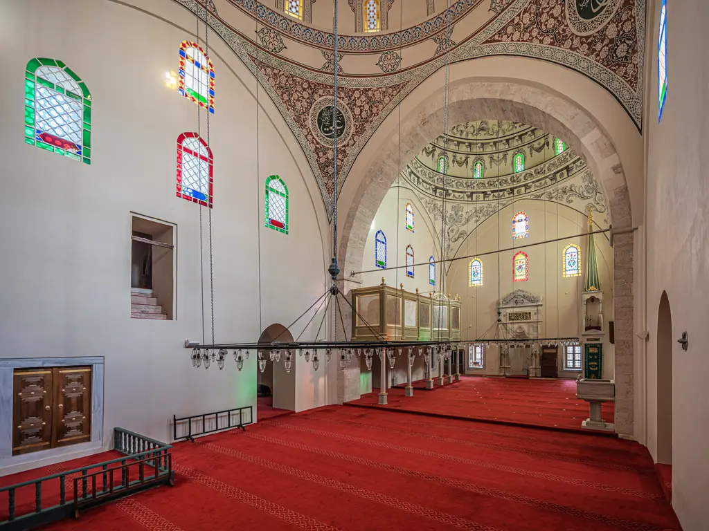 Mahmut Paşa Camii'nin harimi; kırmızı halı, renkli camlı pencereler, kalem işi kemerler, arkada ikinci kubbenin altındaki mihrap ve mahfil.