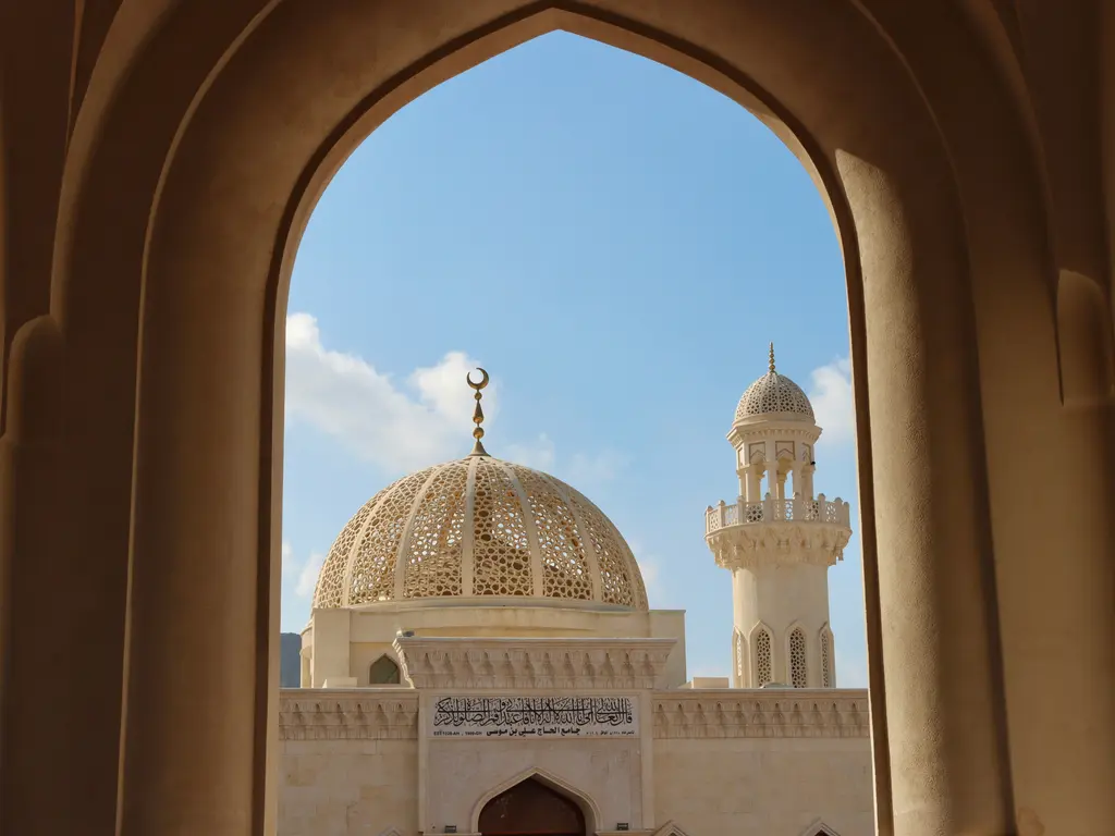 Maskat'ta Sultan Kabus Ulu Camii; büyük sivri kemerin çerçevelediği işlemeli ana kubbe, tepesindeki hilal ve sağda yükselen ince minare.