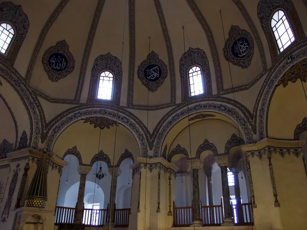 Küçük Ayasofya Camii'nin harimi sıcak ışıkta; yarım kubbe ile kemerlerde mavi gri kalem işi bordürler, hat madalyonları, kemerli pencereler ve altta ahşap korkuluklu galeri açıklıkları.
