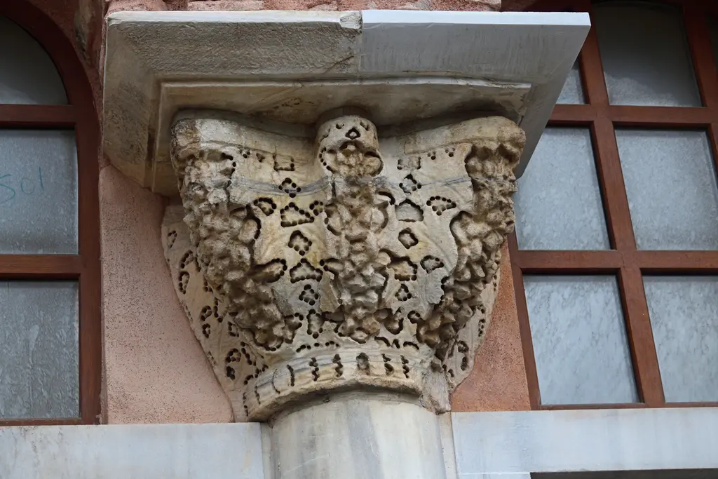 Vefa Kilise Camii'nde bir mermer başlık yakın plan; matkapla derin oyulmuş üzüm salkımları ve akantus yaprakları, üstte sade impost bloğu, çevresinde pembe sıva.