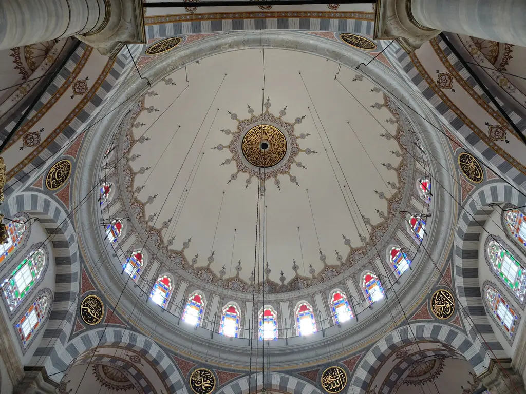 Laleli Camii'nde kubbe içi; merkezdeki rozet, eteğe doğru açılan kalem işleri, kasnaktaki renkli camlı pencere dizisi ve gergi telleri.