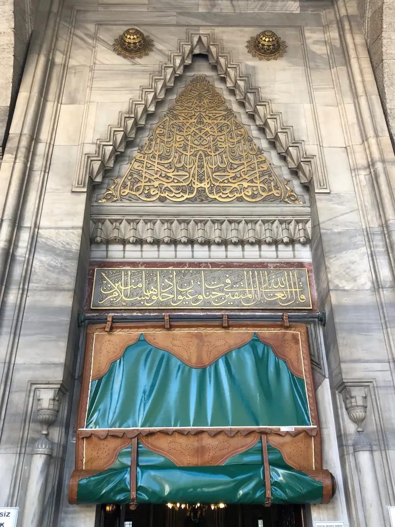 Şişli Camii'nin cümle kapısı; mermer taç, üçgen biçimli altın yazı, altında kitabe kuşağı ve yeşil perdeli giriş.