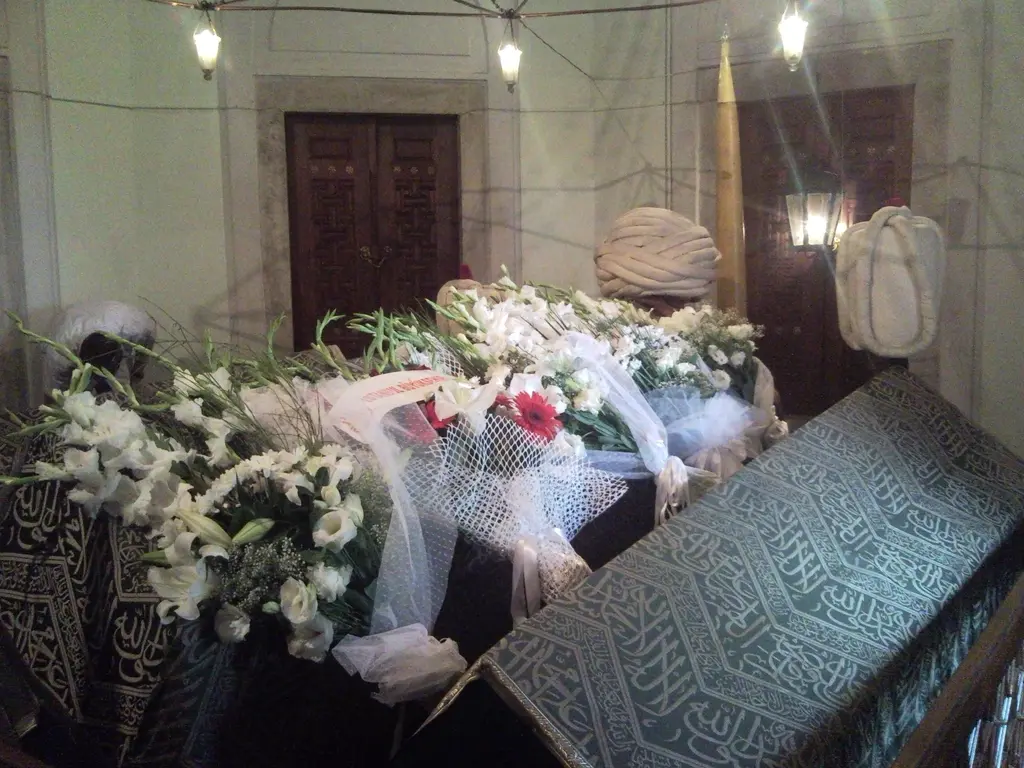 Barbaros Hayreddin Paşa Türbesi'nin içi; yeşil örtülü sandukalar, üzerlerinde çiçekler ve arkada ahşap bir kapı.