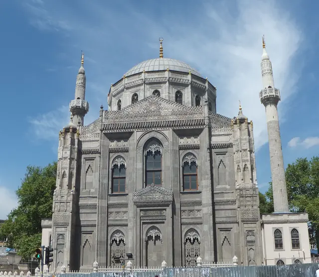 Aksaray'da Pertevniyal Valide Sultan Camii; gri taş cephe, gotik sivri kemerli pencereler, kule gibi köşeler, kurşun kubbe ve iki ince minare.