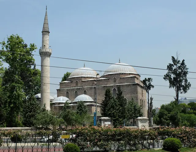 Aksaray'da Murat Paşa Camii; kurşun kaplı kubbeler, kemerli son cemaat yeri, yanında yüksek minare, avludaki ağaçlar ve önde taş duvar.