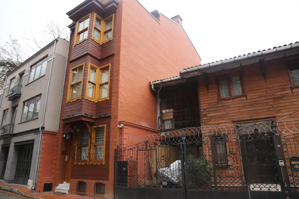 Balat'ta turuncu cepheli cumbalı ev; ahşap kaplama, demir parmaklıklı bahçe kapısı ve yanında beyaz ev.
