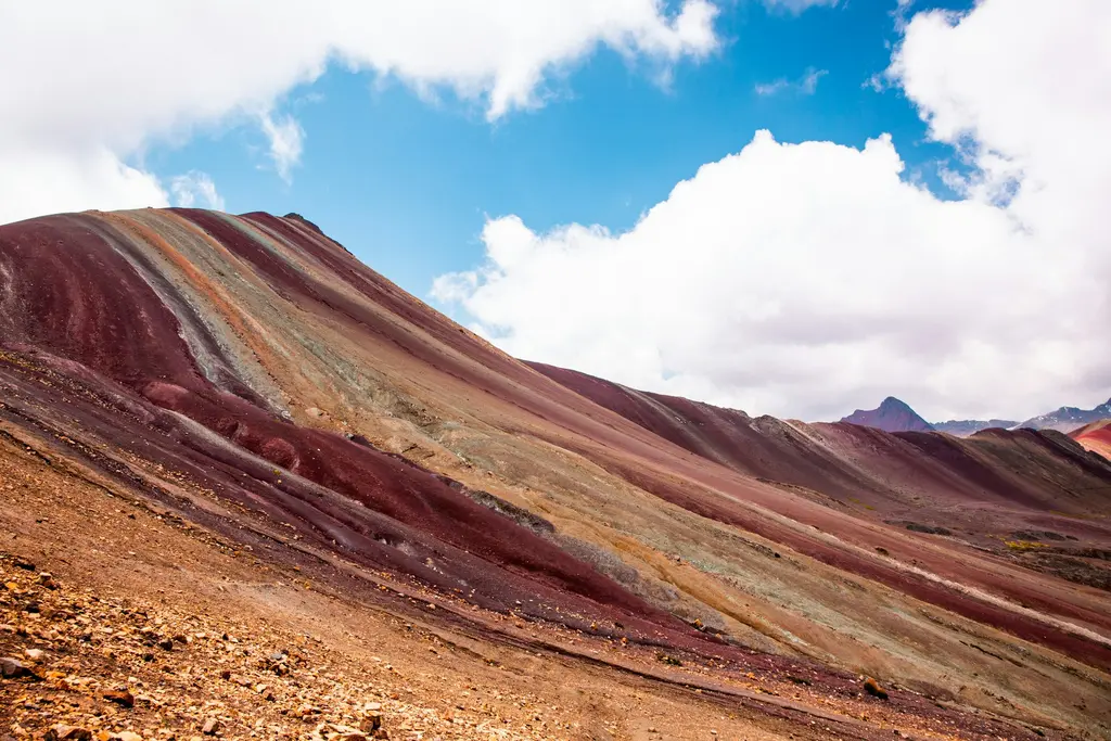 Vinicunca; kırmızı, sarı, yeşil ve mor şeritler hâlinde renklenen dağ yamacı ve karlı And zirveleri.