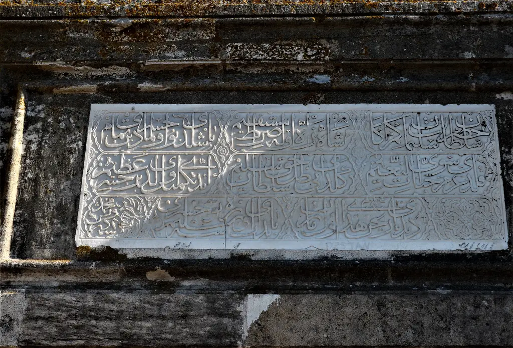 Kanuni Sultan Süleyman Köprüsü'nde kitâbe; taş çerçeve içinde beyaz mermer üzerinde satırlar hâlinde yazı.
